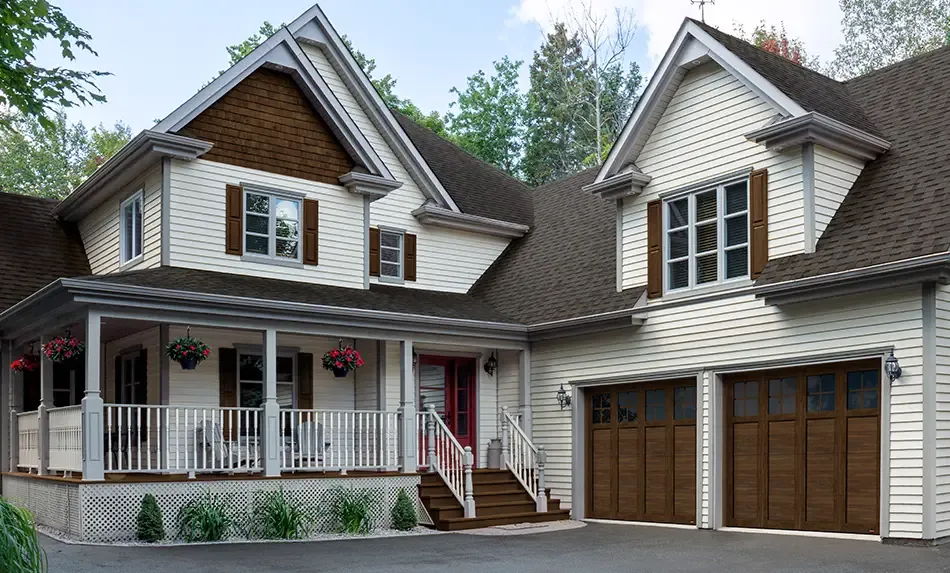 Une maison de style Farmhouse moderne avec des volets couleur bois avec des  portes de garage en acier  et moulures PVC en couleur Faux Bois Noyer chocolaté